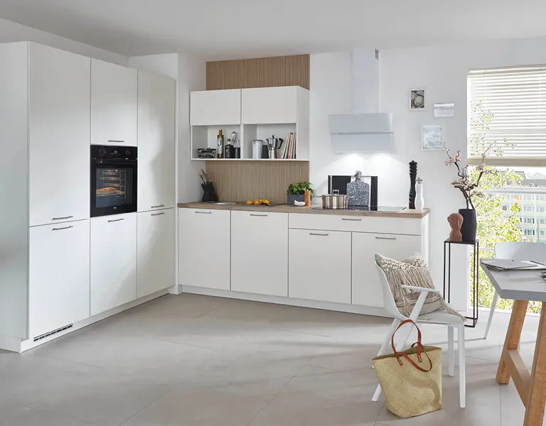 Helle L-Küche in Weiß mit Holzarbeitsplatte, offenen Regalen und modernen Elektrogeräten, kombiniert mit gemütlichem Essplatz und dekorativen Akzenten für zeitgemäßes Küchendesign.